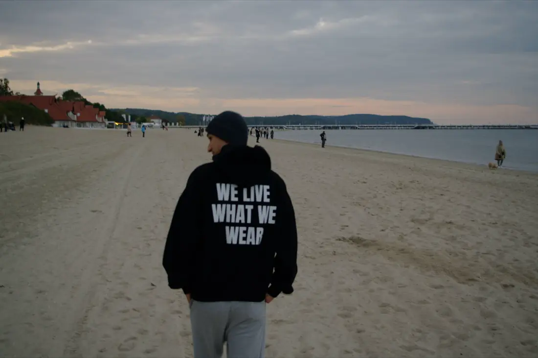 Napis WE LIVE WHAT WE WEAR na plecach, piasek i morze